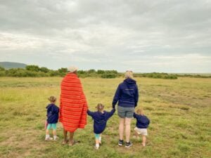 the back of the tour guide, mother, and three little girls all holding hands looking out at trees and a field.