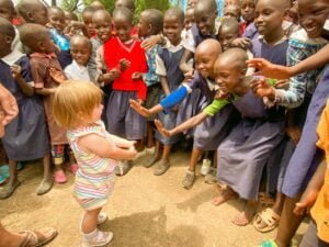 African school aged children high fiving young toddler girl.