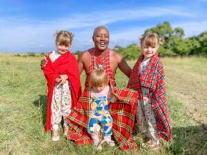 Three little girls wearing red blankets in front of a Masai tour guide in Kenya